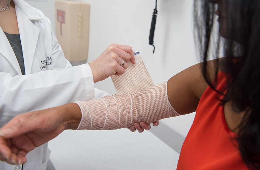 A Cleveland Clinic Caregiver wrapping a bandage around a patient's arm.